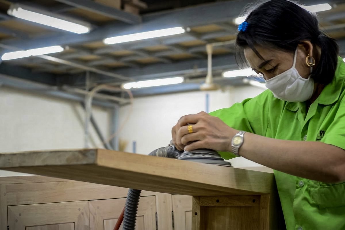 A worker hand-sanding a rubber wood panel during the ISO 9001 quality-control stage at Planet Furniture